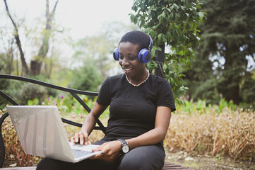 Smiling happy African black short-haired woman student afro hair with blue headphones studying...