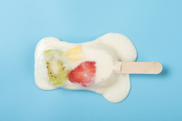 top view yogurt flavor popsicle with slices of kiwi and mango and strawberry melting on blue background