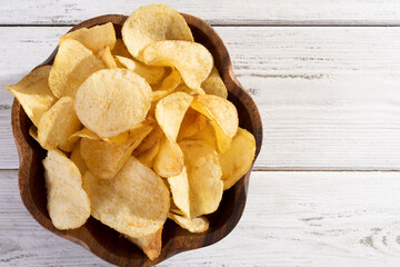 Delicious golden potato chips on a white wooden background.