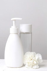 White plastic bottle with dispenser close-up with white flower on a white background, close-up, skin care concept, hair Care, soap and balms, empty space for text