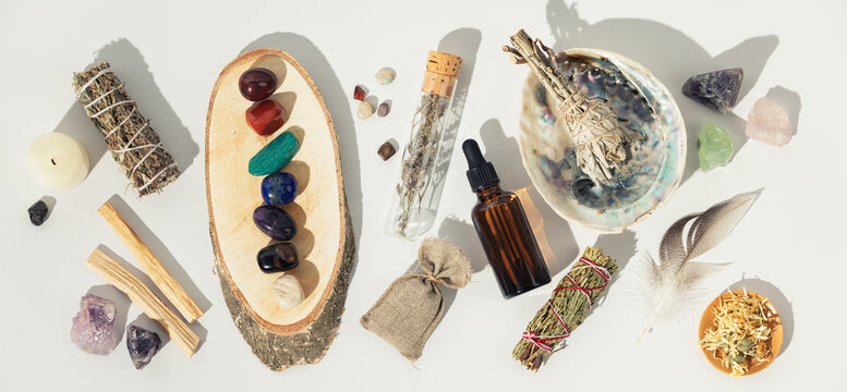 Healing crystals, elixir, palo santo, white sage bundle on abalone sea shell, dry healing herbs on white background