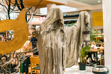 Grim reaper in grey cloak and iron cage for birds stands inside a mall as a decoration. Halloween....