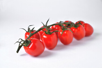 a branch of red cherry tomatoes sharp in front and blurred from behind on a white background, selective focus