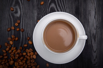 Top view of white cup of creamy coffee on black wooden table with many coffee beans 