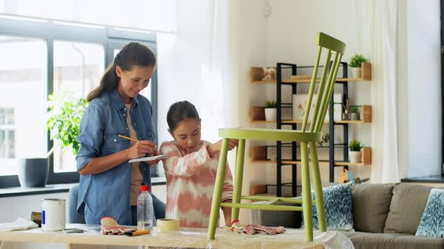family, diy and home improvement concept - happy smiling mother and daughter with ruler measuring old wooden chair for renovation at home