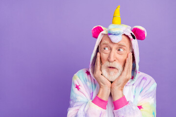 Photo of pretty impressed man pensioner unicorn sleepwear arms cheeks looking empty space isolated violet color background © deagreez
