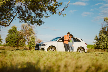 Young multiracial couple using cellphone and standing by car during trip