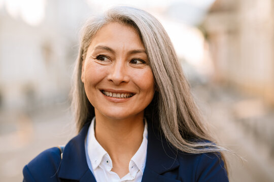 Mature asian woman with grey hair smiling and looking aside