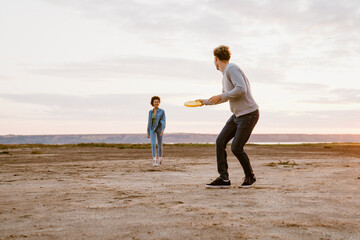 Young multiracial couple smiling while playing with frisbee