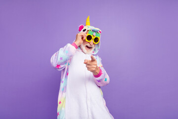 Photo of childish funny man pensioner unicorn sleepwear dark pineapple glasses pointing you isolated violet color background © deagreez