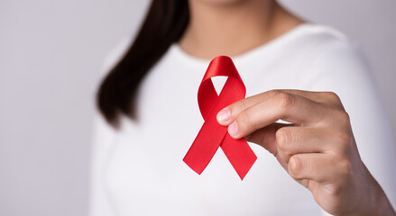 Closeup woman hand holding red ribbon HIV, world AIDS day awareness ribbon. Healthcare and medicine concept. - obrazy, fototapety, plakaty