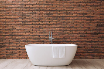 Naklejka na ściany i meble Modern ceramic bathtub with towel near brick wall