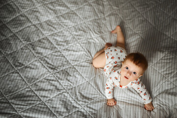 a four-month-old girl crawls on the bed and looks with a surprised look