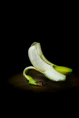 Peeled banana on wooden board black background