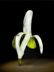 Peeled floationg banana on wooden board black background