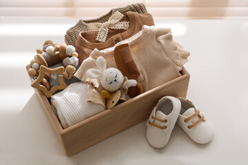 Wooden crate with children's clothes, toys and pacifier near shoes on white table in room