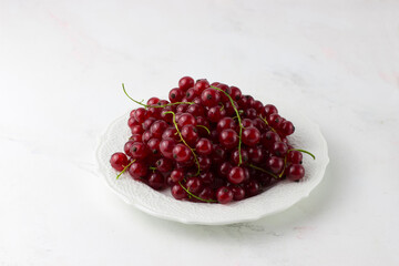 Red currant on a white plate on a white background