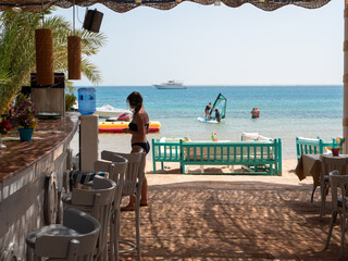 Hurghada, Egypt - September 22, 2021: View of the bar on the beach of the red sea. Girl in a black swimsuit stands near the bar and prepares to place an order.
