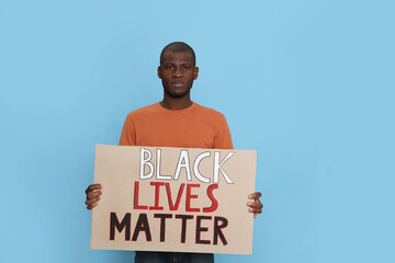 African American man holding sign with phrase Black Lives Matter on light blue background. Racism...