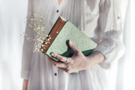 A woman is holding a green book   with flowers on a white background, close up, indoor photography