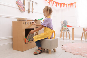 Little girl playing with toy cardboard oven at home
