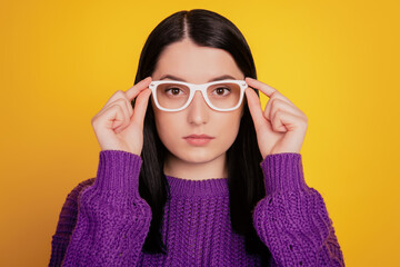 Portrait of serious young girl hand touch glasses confident focused isolated on yellow color background