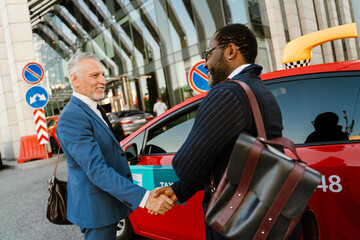 Multiracial men smiling and handshaking while standing by taxi
