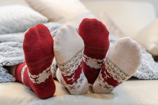 Christmas Socks Of Family Couple Feet Relaxing On Couch Having Good Holiday Time Together, Enjoying Resting At Home In Living Room For Winter Xmas And New Year Day Celebration