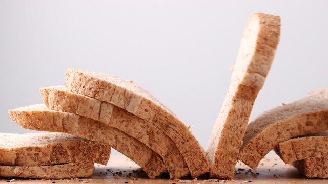Close up whole wheat multigrain bread sliced falling on wooden table on white background, slow motion. Loaf of Bread, Slice of food, Healthy Food Concept.