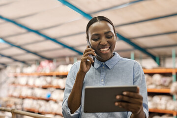 Smiling African woman using a tablet and phone in a warehouse