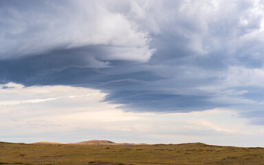 Fototapeta premium Dramatic clouds hover over the golden plains of eastern Kazakhstan, adding depth to the serene steppe landscape