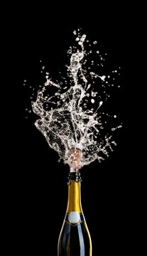 champagne bottle with cork flying with splashing liquid on black.
