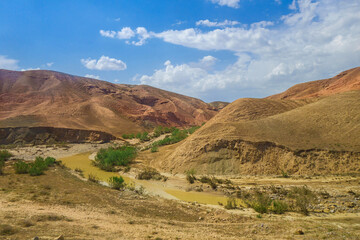 Mountain river, half-dried from the heat of the sun. The channel runs between the mountains and hills scorched by the sun. Nature landscape of Surkhadarya region in South Uzbekistan