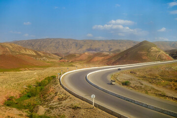 Highway with racing cars in background of hilly valley. Mountains are visible in distance. Shot in Surkhandarya region in Uzbekistan near mountains of Gissar ridge