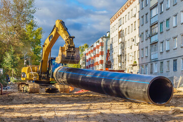Construction work for the replacement or re-laying of engineering pipes. The excavator drags the heat or sewer pipe to the placement site - obrazy, fototapety, plakaty