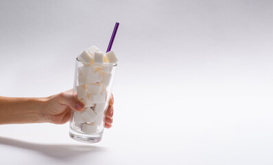 A full glass of sugar cubes in a female hand on a light background. On the right is an empty free...