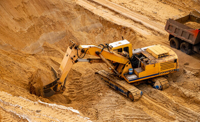 large yellow hydraulic industrial excavator, iron bucket miners, digging and loading sand, inside development of large sandy career.