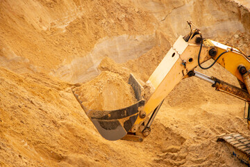 large yellow hydraulic industrial excavator, iron bucket miners, digging and loading sand, inside development of large sandy career.