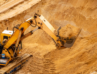large yellow hydraulic industrial excavator, iron bucket miners, digging and loading sand, inside development of large sandy career.