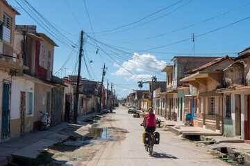 A cyclist moving down a quiet street lined with traditional Cuban buildings, showcasing the simplicity and poorness of local life 