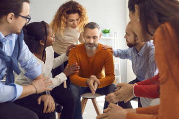 People talking and supporting each other in group therapy session. Multiethnic patients comforting and reassuring upset mature man. Multiracial colleagues show compassion, understanding and empathy