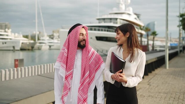 Young caucasian businesswoman talking with arab man, discussing contract terms while walking in port