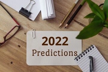 White card with the text 2022 predictions on wooden desk. Health benefits, education, business, job...