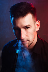 male portrait in color light. a man blowing smoke and holding a hookah pipe