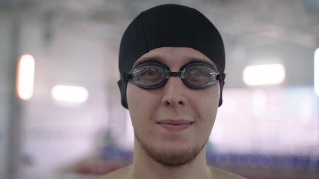 Close uo shot of an Amature sportsman standing near swimming pool and puts on his swimming goggles. Concept of athlete confidence before important competition