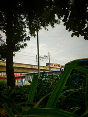 Central Jakarta, Indonesia - April 5th, 2021: The electric train was speeding and framed by trees and grass, the train line was close to the istiqlal mosque.