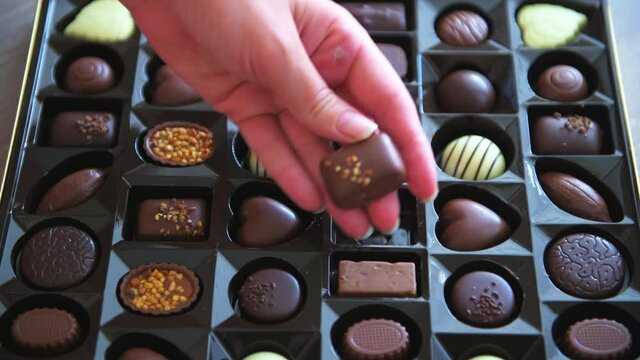 Female woman hand taking choosing picking truffle from packaged box of chocolates with luxury gourmet milk and dark desserts package macro closeup and different shapes variety