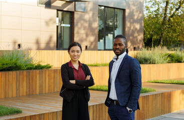 Business partners African American man in formal suit and young Asian woman with long brunette hair stand near office in backyard