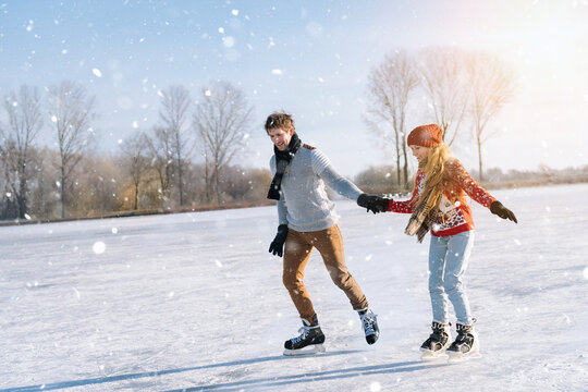 Loving couple in warm sweaters having fun on ice. Woman and man ice skating outdoors in sunny snowy day. Active date on ice arena in winter Christmas Eve. Romantic activities and lifestyle concept