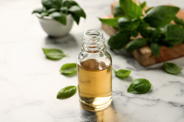 Glass bottle of basil essential oil and leaves on white  marble table